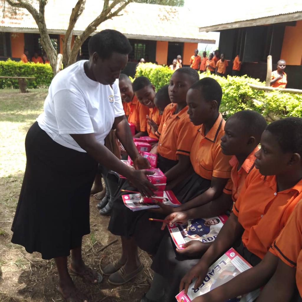 A TAGI facilitator handing menstrual products to students seated outdoors